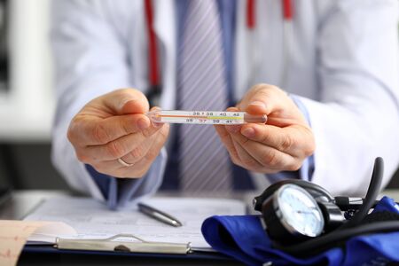 Male doctor holding in hand thermometer indicating high temperature close-up