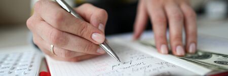 Close-up view of woman managing domestic budget and writing all down in notebook. Monthly income and...