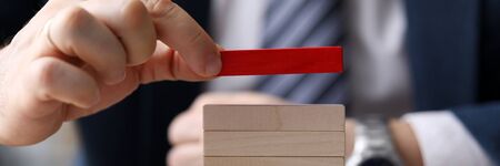 Close-up view of businessman holding one red cube and putting on tower of light wooden blocks. Selective focus on bars. Leadership and uniqueness conceptの写真素材
