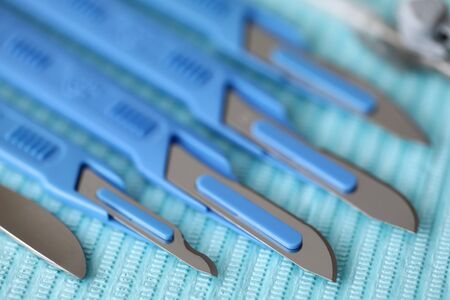 Close-up of surgical instruments in operating room on blue sterilized wrap. Different knifes for...