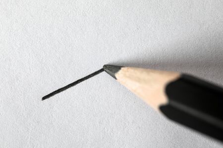 Close-up of black graphite pencil drawing perfectly straight line on textured white sheet. Short direct distance on piece of paper. Art and painting conceptの写真素材