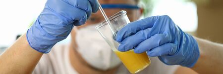 Close-up of worker in respirator dripping liquor drops to beaker with wood varnish. Specialist in...