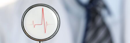 Male medicine doctor arm holding stethoscope head closeup in front of his chest. Medic shop or...
