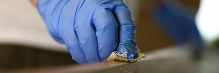 Close-up of male hand in protective glove varnishing wooden surface at workshop. Special lacquer covering. Carpentry work and joinery processing conceptの写真素材