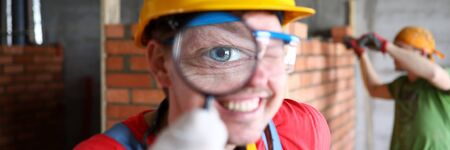 Smiling builder in uniform carefully examining finished job with magnifier closeup. Professional and high quality home renovation conceptの写真素材
