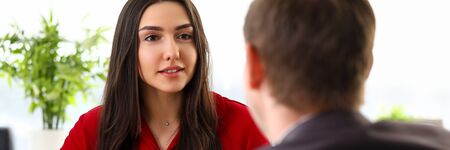Young beautiful businesswoman in stylish official clothes sitting in office and talking with man...