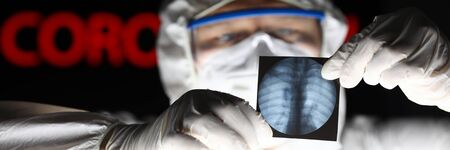 Male doctor wearing protective suit mask and gloves looking at xray shot detecting problem close-up