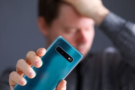 Pensive man holding an hand broken expensive modern smartphone close-up