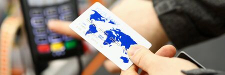 Male hand holding banking card while paying with it at cash desk of supermarket close-up