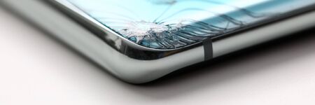 Modern smartphone lying at table with crack in corner close-up