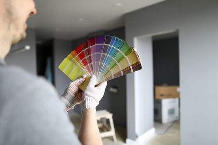 Repairman in gloves standing in flat, looking at walls and trying to choose color for interior...