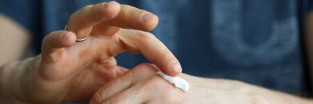 Male hands applying moistening cream on skin closeup