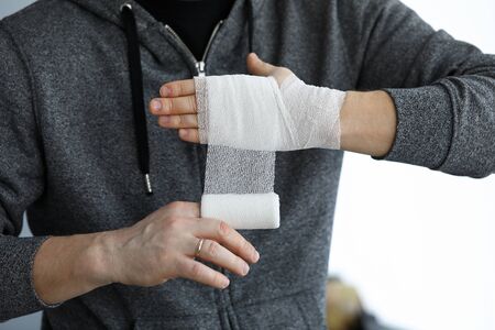 Man give himself first aid rolling bandage tape over wrist close-up