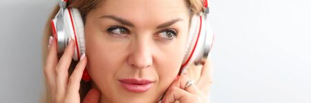 Portrait of beautiful female in modern headphones looking away thoughtfully. Music lover enjoying...