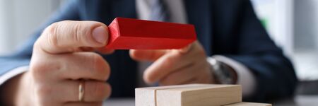 Man builds on table construction wooden blocks. Options for solving problem. Need for respect and recognition. Desire to build connections in society. Actualization factors for specific situationの写真素材