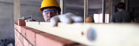 Construction guy helmet measures level brickwork. Level is used when laying bricks in order to check verticality. High quality and stable reading. Indoor use equipment. Smooth brickworkの写真素材