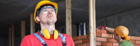 Builder in overalls and helmet makes notes folder. Brick specifications. Builder calculates height using special table. Duration commissioning facility. Construction errors. Fine finishの写真素材