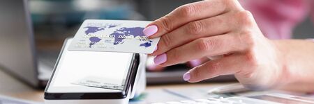Close-up of female hand holding credit card. Manager helping pay for service using terminal....