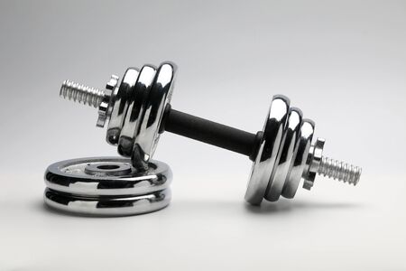 Silver coloured shiny metal dumbbell standing at pile of disks close-upの写真素材