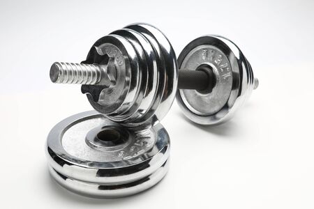 Silver coloured shiny metal dumbbell standing at pile of disks close-upの写真素材