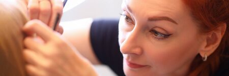Close-up of professional makeup artist correcting clients eyebrow. Macro shot of concentrated face...
