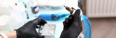 Close-up of professional cosmetologist holding container with light brown paint colour. Woman working in protective gloves. Permanent makeup and beauty salon conceptの写真素材