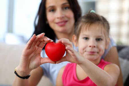 Focus on hands of happy mother and little daughter hands holding toy red heart. Love relationship between mum and child. Friendly family and motherhood conceptの写真素材
