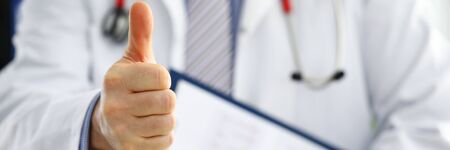 Male medicine doctor holding document pad in hand showing OK or approval sign with thumb up. High...
