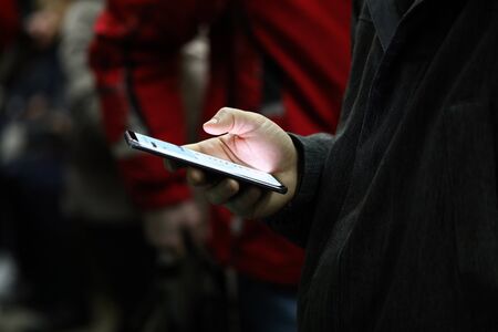 Close-up of persons hand holding mobile phone with light screen. Man scrolling news or playing game. Kill time and entertainment in public transport conceptの写真素材