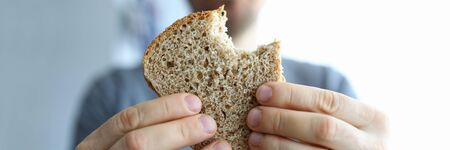 Close-up of person holding slice of fresh whole wheat bread. Male showing tasty rye. Bakery and...