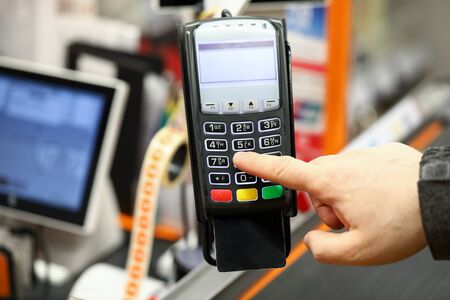 Male hand typing pin code card while paying with it at cash desk of supermarket close-up