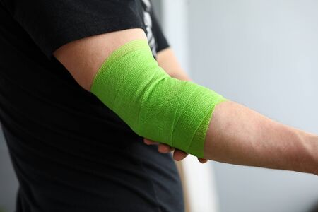 Man shows stretching on arm with elastic bandage. Bandage for people leading an active lifestyle, athletes as a prevention sprains and injuries. Elastic bandage on elbow joint with compression effectの写真素材