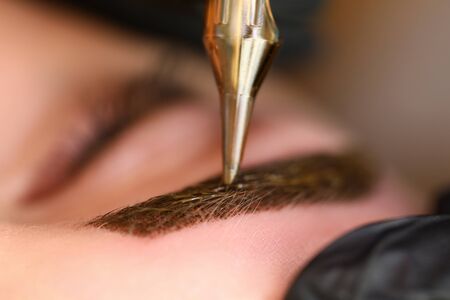 Close-up of special beauty equipment applying light brown colour on prepared eyebrow. Macro shot of...