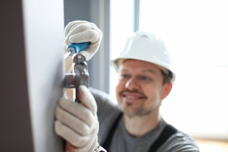 Close-up of mans hands scroll detail with screwdriver instrument. Smiling worker wearing white helmet for work. Foreman busy with door. Construction site and handyman conceptの写真素材