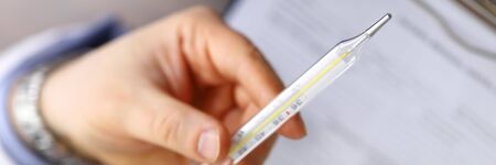 Male doctor holding in hand thermometer indicating high temperature close-up