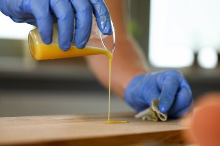 Close-up of woodworker hands in gloves pouring over wood varnish on wooden surface. Man covering furniture with special polishing fluid. Joinery processing conceptの写真素材