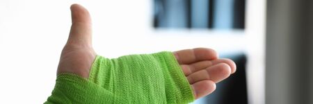 Close-up of person ties up hand with green ace bandage. Fracture bone and x ray image of break wrist. Injury or accident. Modern medicine and long recovery conceptの写真素材