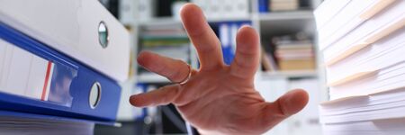 Close-up of businessman hand reaching out for paper folder. Stacks of documents on left and right...