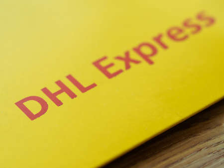 Barcelona, Spain - May 01, 2020: Red DHL sign over yellow envelope carton close-up