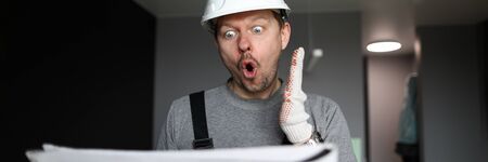 Portrait of engineer looking at plan of construction or plan. Emotional handyman or contractor with paper of working tasks. Renovation of home, service for interior renewalの写真素材