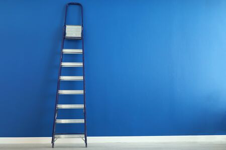 Close-up of metal ladder standing on blue wall. Equipment for worker to paint wall. Copy space in right side. White floor. Construction site and renovation conceptの写真素材