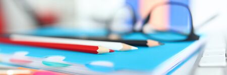 Close-up of bright colourful pencils on table. Blue notebook for creative ideas and thoughts. Black glasses. Working desktop with stuff. Mess on clerk desk. Business conceptの写真素材