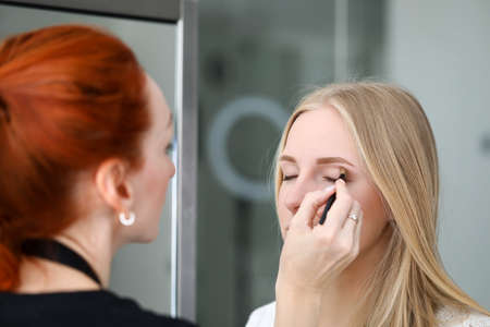 Portrait of professional makeup artist applying lipstick with special equipment. Young beautiful...