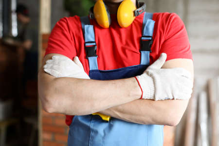 Close-up of male person standing with folded hands. Professional builder in special boilersuit....