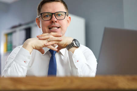 Portrait of businessman in glasses looking at camera with calmness. Employee working on laptop in...