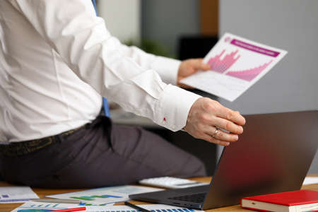 Close-up of executive manager sitting on table in office. Male person working on laptop. Businessman...