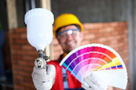 Close-up of smiling construction site worker holding colourful palette with samples and empty...