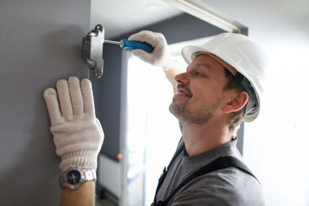 Portrait of smiling happy handyman fixing interconnecting door with special equipment. Professional repairman using screwdriver for renovation. Refurbishment conceptの写真素材