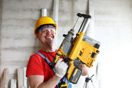 Portrait of smiling builder in boilersuit, protective glasses and helmet. Repairman using building...