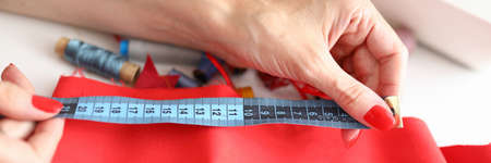 Close-up of female dressmaker using blue tape measure for work with textile. Fabrics for red dress....